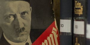 Eine Ausgabe des Buches "Mein Kampf" wird aus einem Bücherregal gezogen. Auf dem Cover ist das Gesicht Adolf Hitlers zu sehen