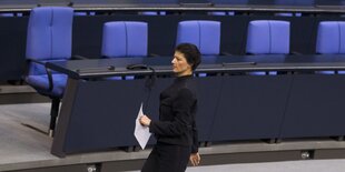 Sarah Wagenknecht geht vor blauen Stuhlreihen alleine durch den Raum