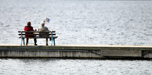 Zwei alte Leute sitzen auf einer Bank und blicken aufs Wasser