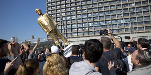 eine Menschenmenge kippt eine goldene Statue