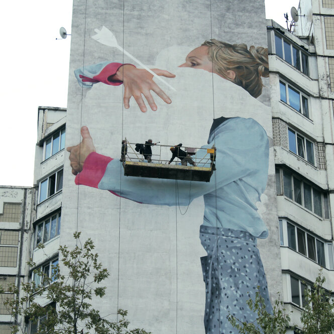 Ein BIld auf einem Hochhaus zeigt eine Frau, die einen weißen Schatten mit einem Pfeil im Rücken umarmt