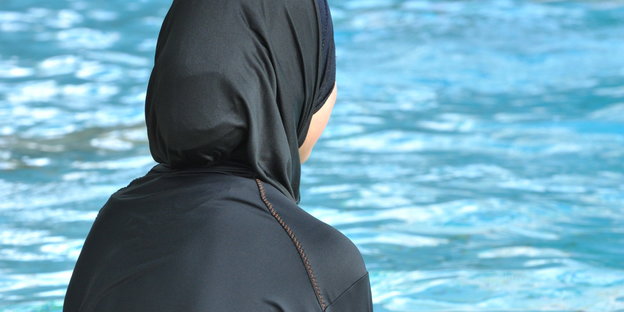 Ein Mädchen sitzt im Burkini in einem Schwimmbad