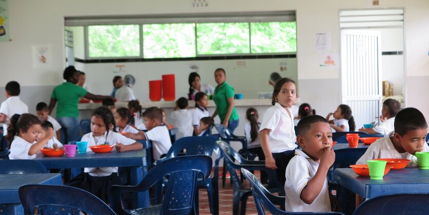 Kinder in Schuluniform sitzen in der Schulkantine an Plastiktischen und essen