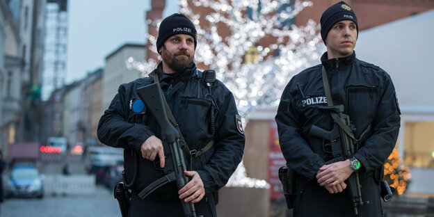 Polizisten mit Maschinenpistolen stehen vor einem Weihnachtsmarkt