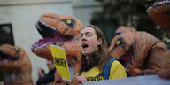 Ein Mann hält ein gelbes Schild in der Hand, um ihn herum stehen Menschen in Dinosaurierkostümen