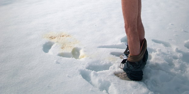 Ein Mann mit heruntergelassener Hose pinkelt in den Schnee