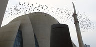 Ein Vogelschwarm fliegt um eine Moschee