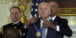 Obama steht hinter Biden und legt ihm die Medaille um den Hals