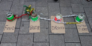 Vier Dosen mit den Aufschriften „Food“, „Bier“, „Drogen“ und „Plattentiere“, stehen nebeneinander auf dem Boden