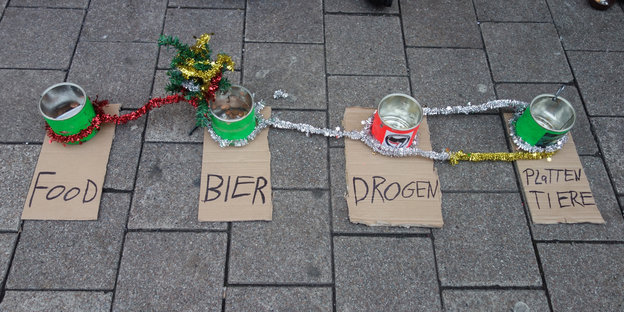 Vier Dosen mit den Aufschriften „Food“, „Bier“, „Drogen“ und „Plattentiere“, stehen nebeneinander auf dem Boden