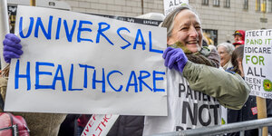 Eine Frau hält ein Plakat hoch. Darauf steht: „Universal Healthcare“