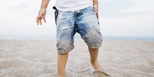 Ein Kind spielt in einer Jeans am Strand