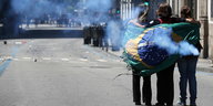 Drei Menschen haben sich in eine brasilianische Fahne eingehüllt, um sie herum weht Rauch