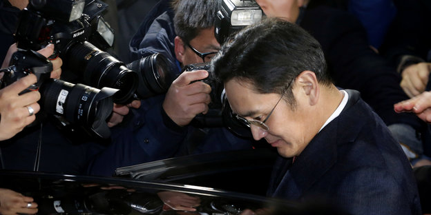 Lee Jae Yong ist umringt von Fotografen. Gesenkten Hauptes steigt er in ein Auto ein
