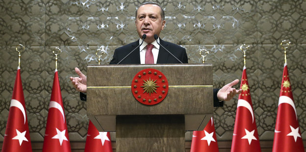 ein Mann steht an einem Rednerpult, davor mehrere türkische Fahnen