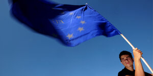 Ein junger Mann hält eine EU-Flagge vor blauem Himmel.