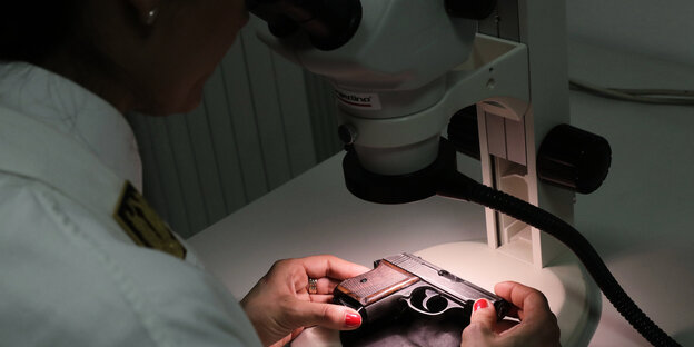 Eine Frau untersucht eine Pistole mit einem Mikroskop