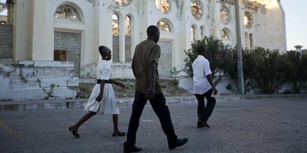 Drei Menschen laufen an der Ruine einer Kathedrale in Port-au-Prince, Haiti, vorbei