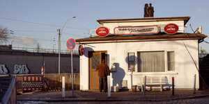 Ein kleines Häuschen steht am Straßenrand. Über dem EIngang steht auf einem Schild "Veddeler Fischgaststätte"