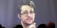 Edward Snowden guckt als Projektion von einer Leinwand ins Publikum