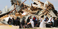 Verschleierte Frauen sitzen vor einem großen Trümmerhaufen