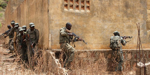 Soldaten mit Gewehren drücken sich an eine Hauswand