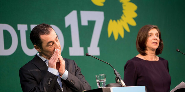 Cem Özdemir und Katrin Göhring-Eckhardt stehen vor dem Grünen-Logo. Cem Özdemir putzt sich die Nase