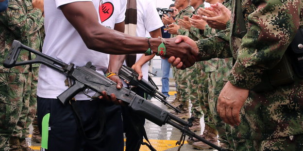 Ein Mensch mit Waffe gibt einem anderen Menschen in Soldaten-Uniform die Hand
