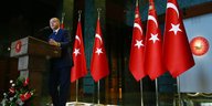 Foto aus der Froschperspektive: Ein Mann in Anzug an einem Podest, hinter ihm türkische Nationalflaggen