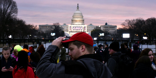 Ein Mann mit einer roten Schirmmütze steht vor dem Capitol-Gebäude in Washington D.C.