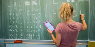 Ein Mädchen steht mit einem Tablet vor einer Schultafel