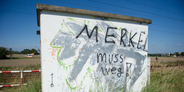 An einer Betonwand vor einer Wiesenlandschaft steht der Schriftzug "Merkel muss weg"