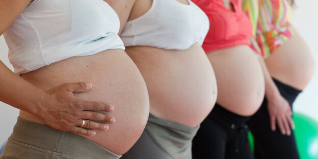 Es sind vier schwangere Frauen im Profil zu sehen, die leicht versetzt nebeneinander stehen. Ihre Träger-Shirts sind hochgekrempelt, so dass ihre nackten Bäuche zu sehen sind