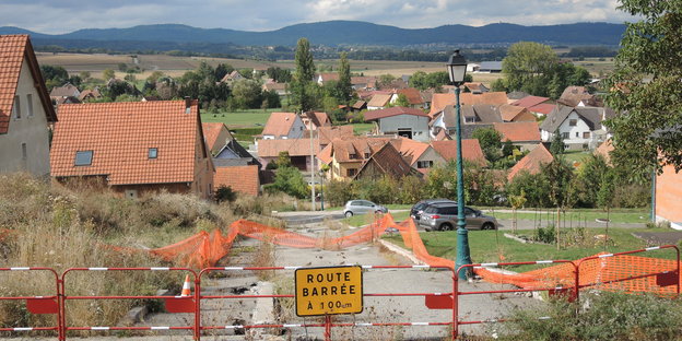 Eine gesperrte Straße, dahinter ein Dorf, am Horizont Berge