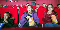 Kinder sitzen in roten Kinosesseln und essen Popcorn