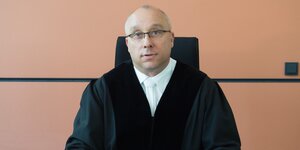 Richter Jens Maier sitzt an einem Pult und blickt in die Kamera