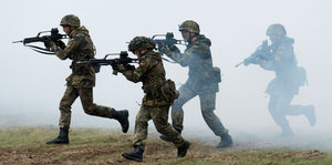 Soldaten in Uniform rennen mit Gewehren in den Händen durch den Nebel