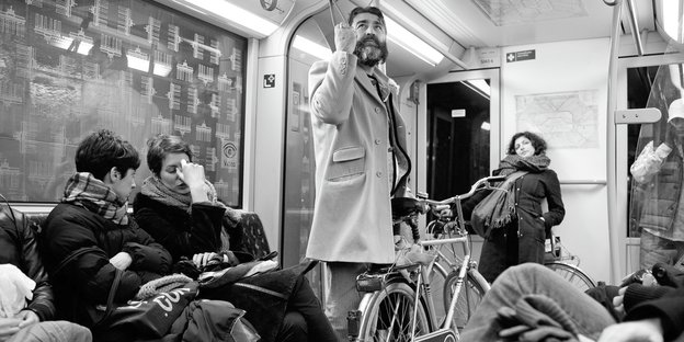 In einer U-Bahn: Zwei Frauen sitzen, ein Mann hält sich am Griff fest und steht