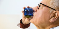Ein Mann trinkt Olivenöl aus einem blauen Glasgefäß.