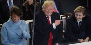 Melania, Donald und Barron Trump sitzen nebeneinander und lachen