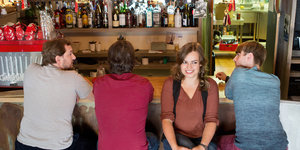 Die Sängerin Fee Badenius sitzt gemeinsam mit ihren Musikern an einer Bar.