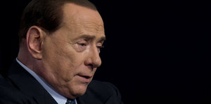 Berlusconi in schwarzem Jackett vor schwarzem Hintergrund guckt sorgenvoll