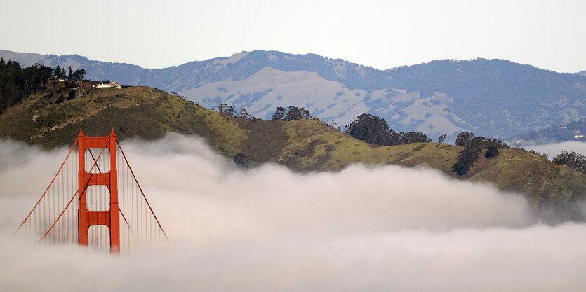 Ein roter Pfeiler der Golden Gate Bridge ragt aus einem dicken weißen Wolkenteppich