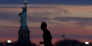 die Silhouette eines Mannes vor der in der Abenddämmerung verschwimmenden Freiheitsstatue