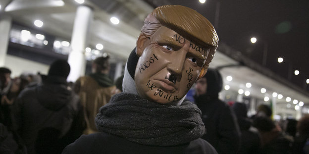 Jemand trägt auf dem Hinterkopf eine Trump-Maske mit einem Hitlerbärtchen