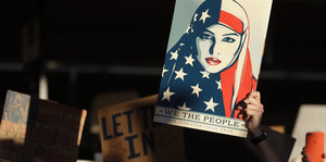 Ein Plakat zeigt eine Frau mit Kopftuch, welches das Muster der USA-Flagge hat