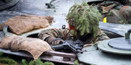 Ein Soldat mit Schminke im Gesicht und Tannenzweigen auf dem Kopf schaut aus einer Panzerluke