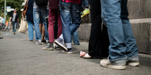 Menschen stehen in einer langen Schlange, man sieht nur die Beine, die sich aneinanderreihen