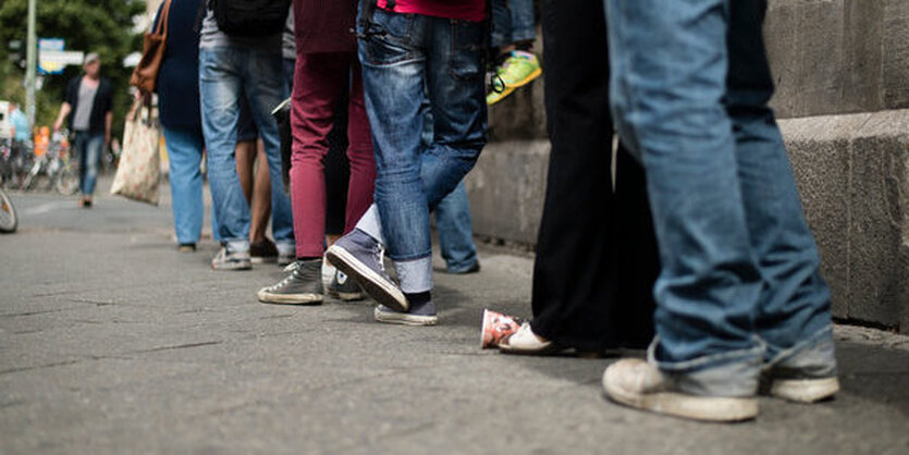 Menschen stehen in einer langen Schlange, man sieht nur die Beine, die sich aneinanderreihen