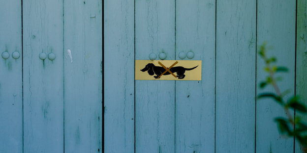 Auf einer blauen Holzwand ist ein Schild mit einem durchgestrichenen Dackel